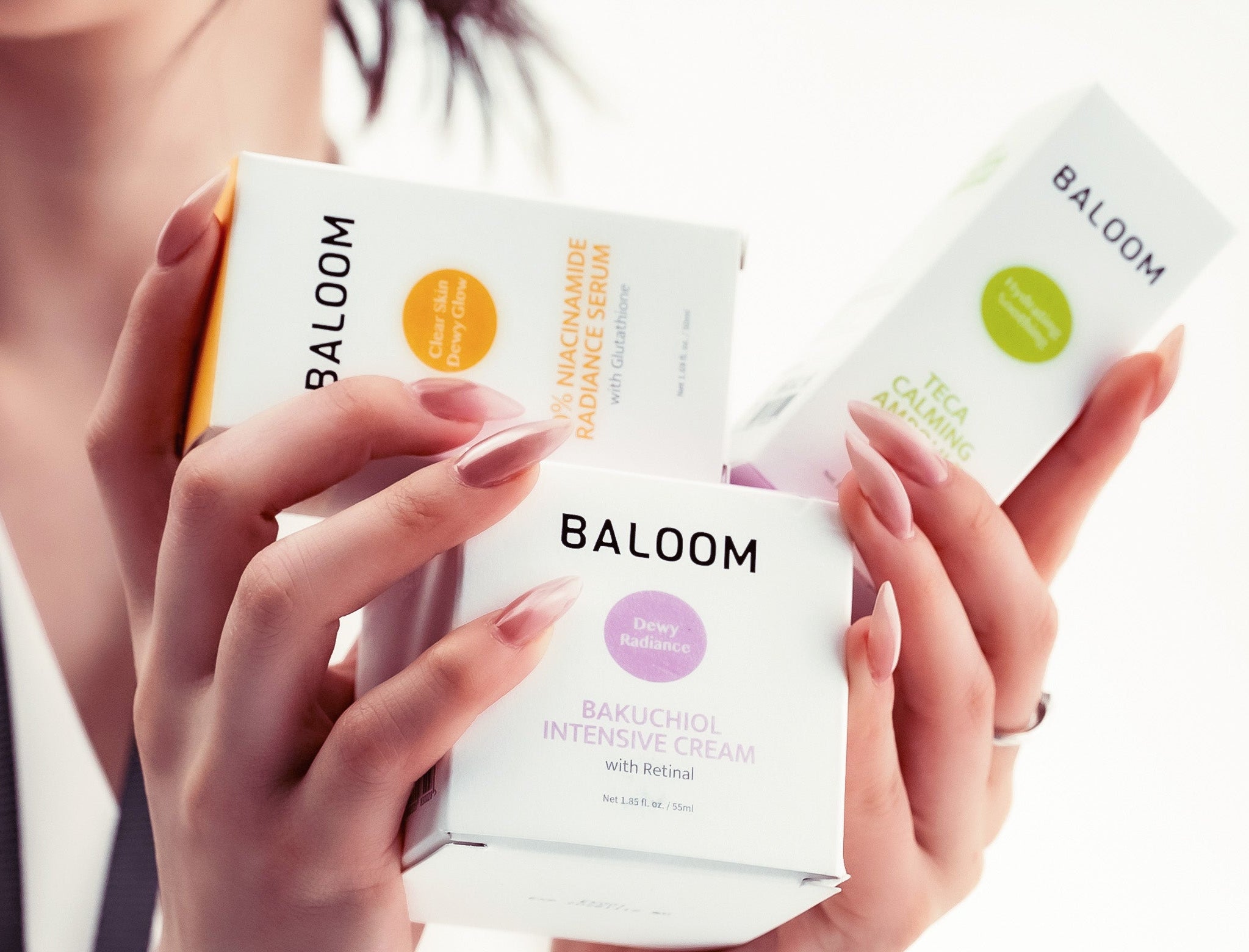 Hands holding Baloom skincare products against a white background
